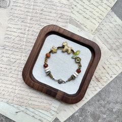 Meadow Pup Bracelet — flat lay in a wooden tray on vintage papers; warm amber and neutral beads with puppy, leaf, star, and floral accents
