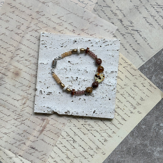 Speckled Honey Heart Bracelet — flat lay on layered vintage papers; warm honey and neutral beads with a speckled heart accent and magnetic clasp