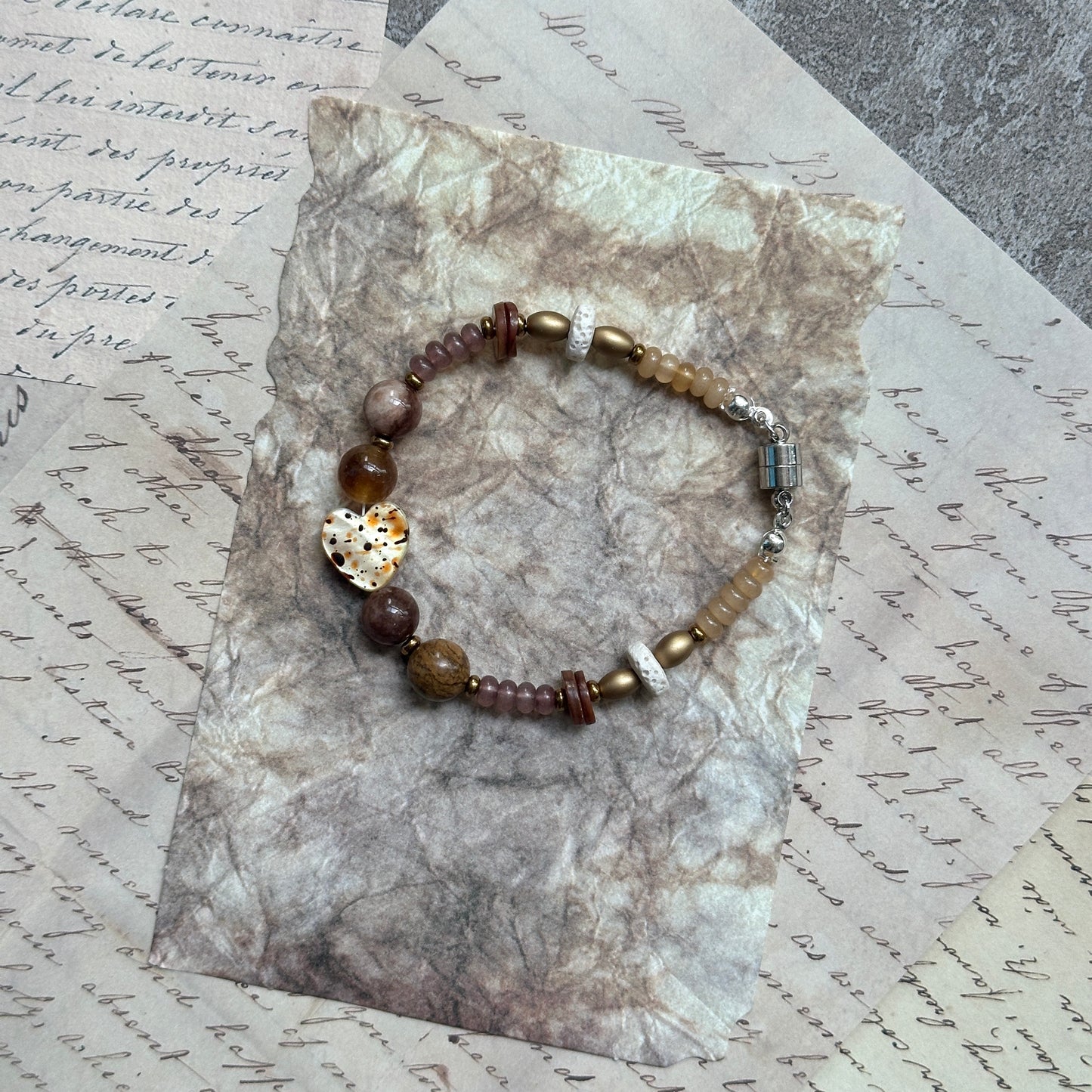 Speckled Honey Heart Bracelet — circle layout on textured background showing warm neutral palette and heart focal