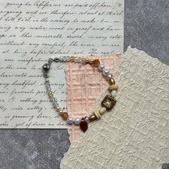 Olive Sunburst Bracelet — flat lay in a wooden tray on textured papers; honey and pearl beads with an olive square sunburst charm, red leaf accent, and magnetic clasp 3