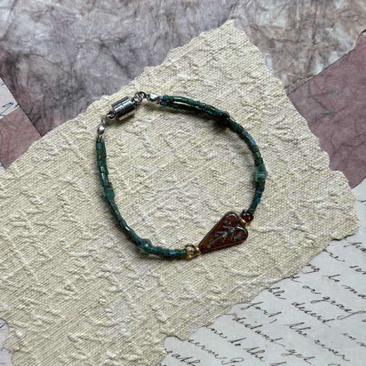 Verdant Talisman Bracelet — flat lay on textured papers; deep forest-green beads with a botanical heart talisman and magnetic clasp