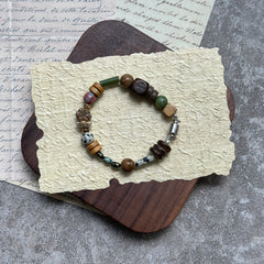 Cedar & Sage Bracelet — flat lay on textured papers and wooden tray; cedar-brown and sage-green beads with speckled jasper accents and a magnetic clasp
