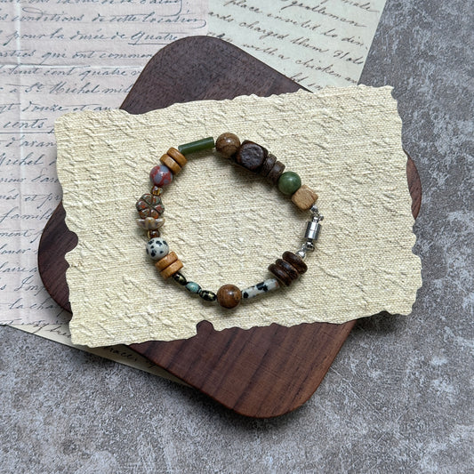 Cedar & Sage Bracelet — flat lay on textured papers and wooden tray; cedar-brown and sage-green beads with speckled jasper accents and a magnetic clasp