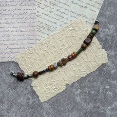 Cedar & Sage Bracelet — flat lay on textured papers and wooden tray; cedar-brown and sage-green beads with speckled jasper accents and a magnetic clasp 3