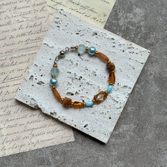 Aqua & Amber Drift Bracelet — flat lay on textured stone paper; sea-glass aqua and warm amber beads with gold accents and a nickel-free magnetic clasp