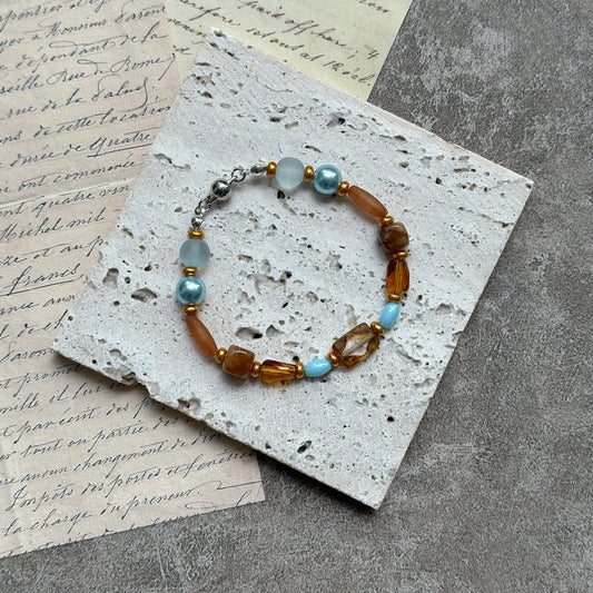Aqua & Amber Drift Bracelet — flat lay on textured stone paper; sea-glass aqua and warm amber beads with gold accents and a nickel-free magnetic clasp