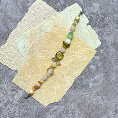 Citron Bloom Bracelet — flat lay on layered yellow papers; lemon-yellow and olive-green beads with citrus-style focal and leaf accents