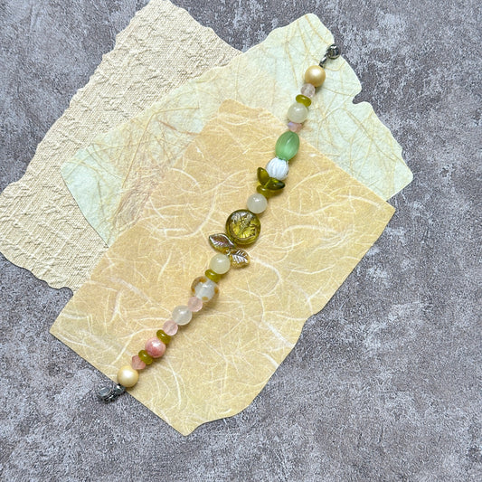 Citron Bloom Bracelet — flat lay on layered yellow papers; lemon-yellow and olive-green beads with citrus-style focal and leaf accents