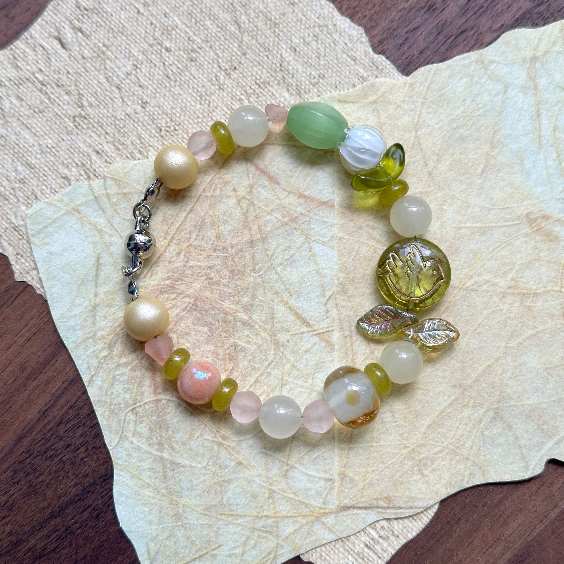 Citron Bloom Bracelet — flat lay on layered yellow papers; lemon-yellow and olive-green beads with citrus-style focal and leaf accents 2