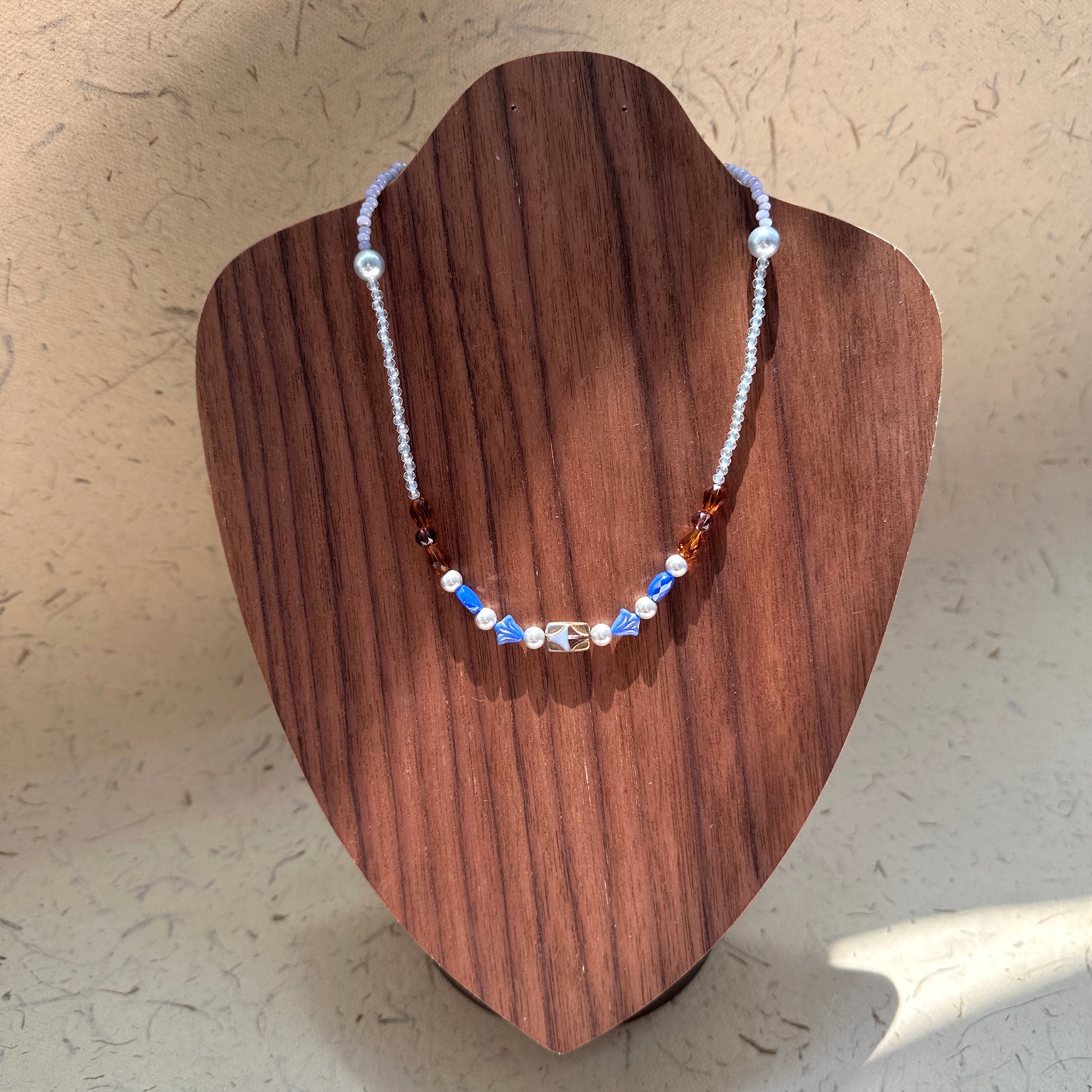 Amber Ocean Necklace on wood display bust — alternating amber and sapphire-blue glass beads