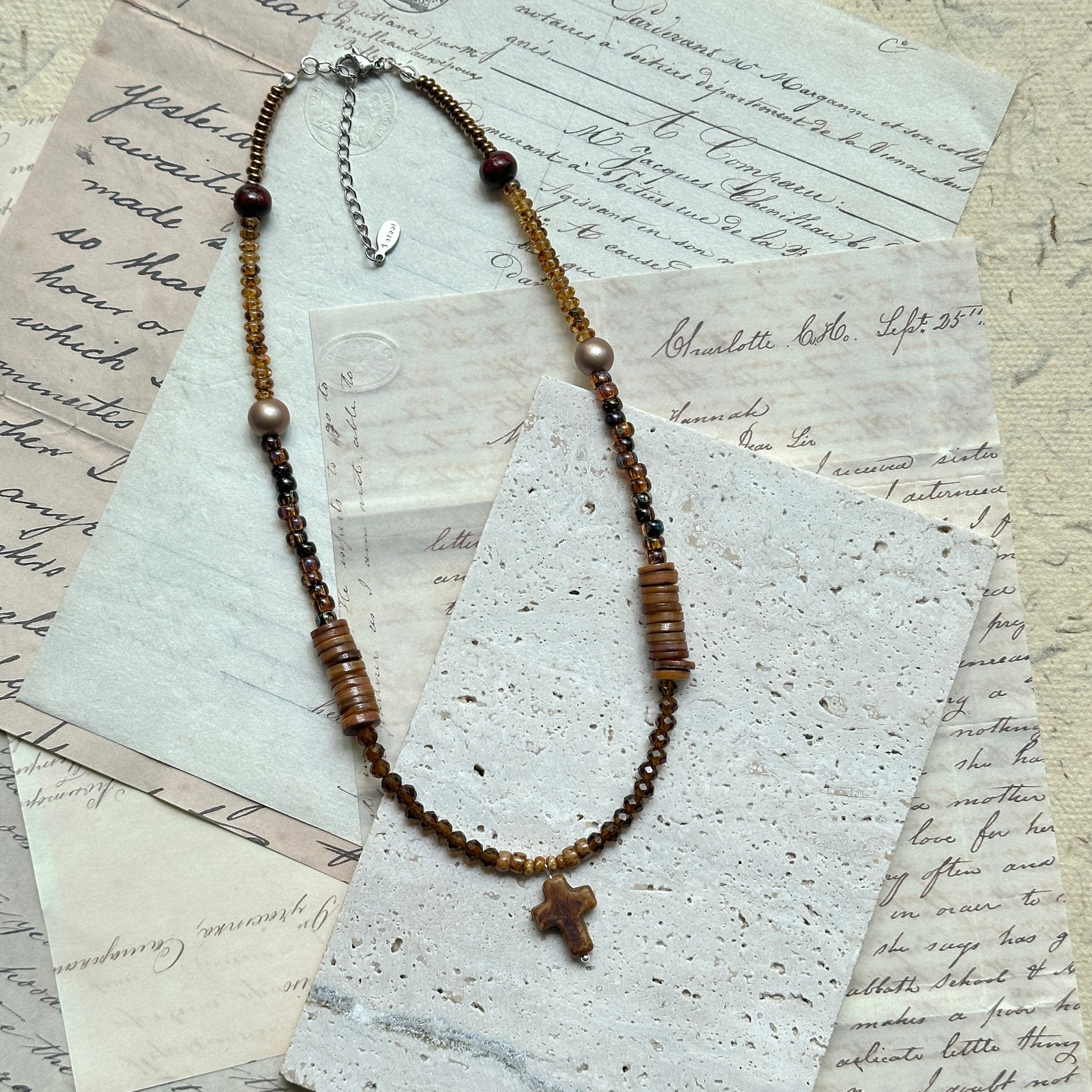 Amber Cross Necklace — circle layout on textured paper showing bead tones, pearl detail, and cross charm