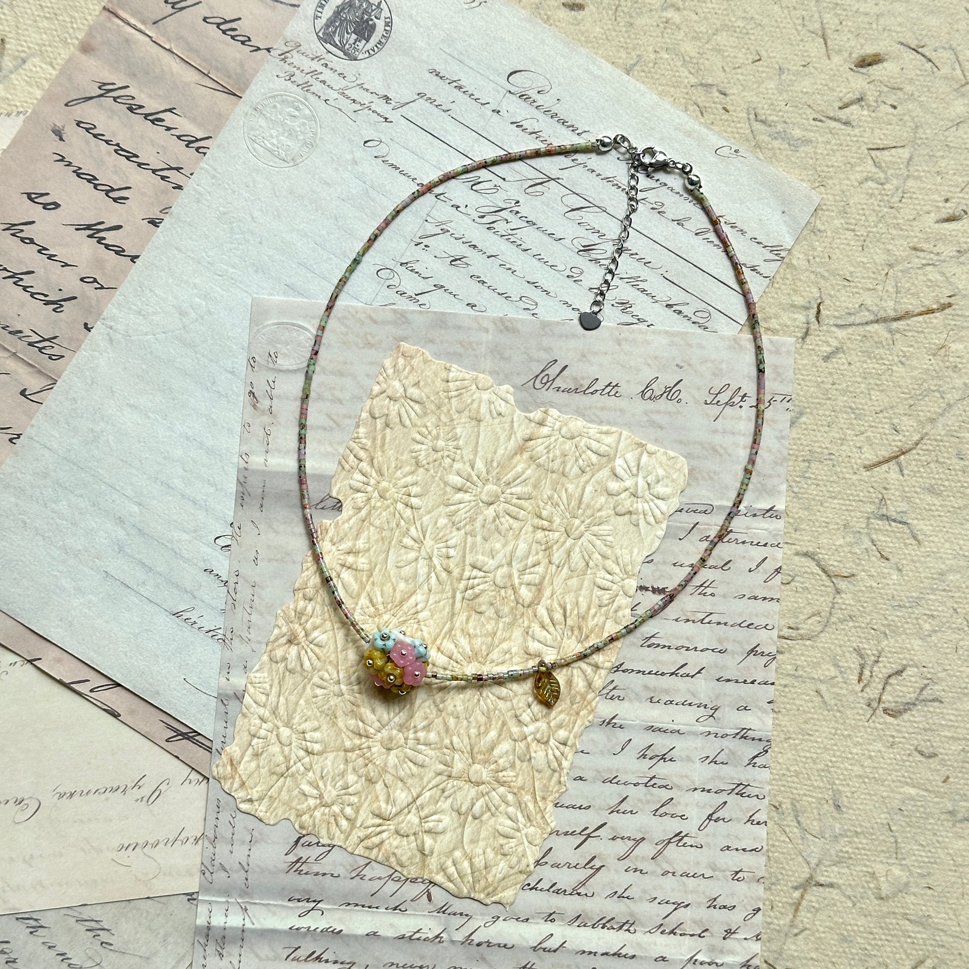 Blossom Garden Necklace — circle layout on textured paper; delicate multicolor seed beads with golden leaf charm