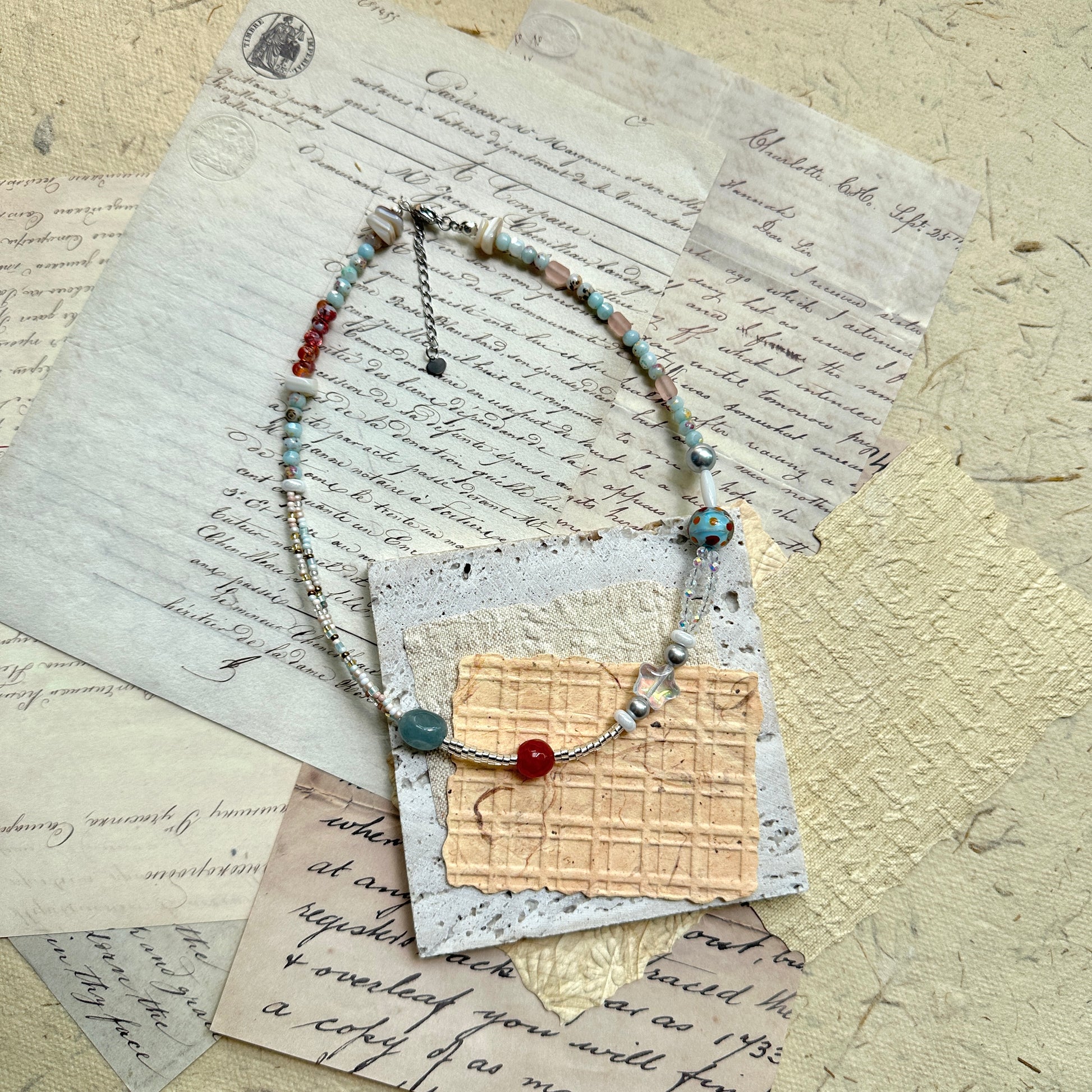 Candy Sky Necklace — flat lay on vintage papers; pastel glass beads with red and blue accents, star charm, polka-dot lampwork bead