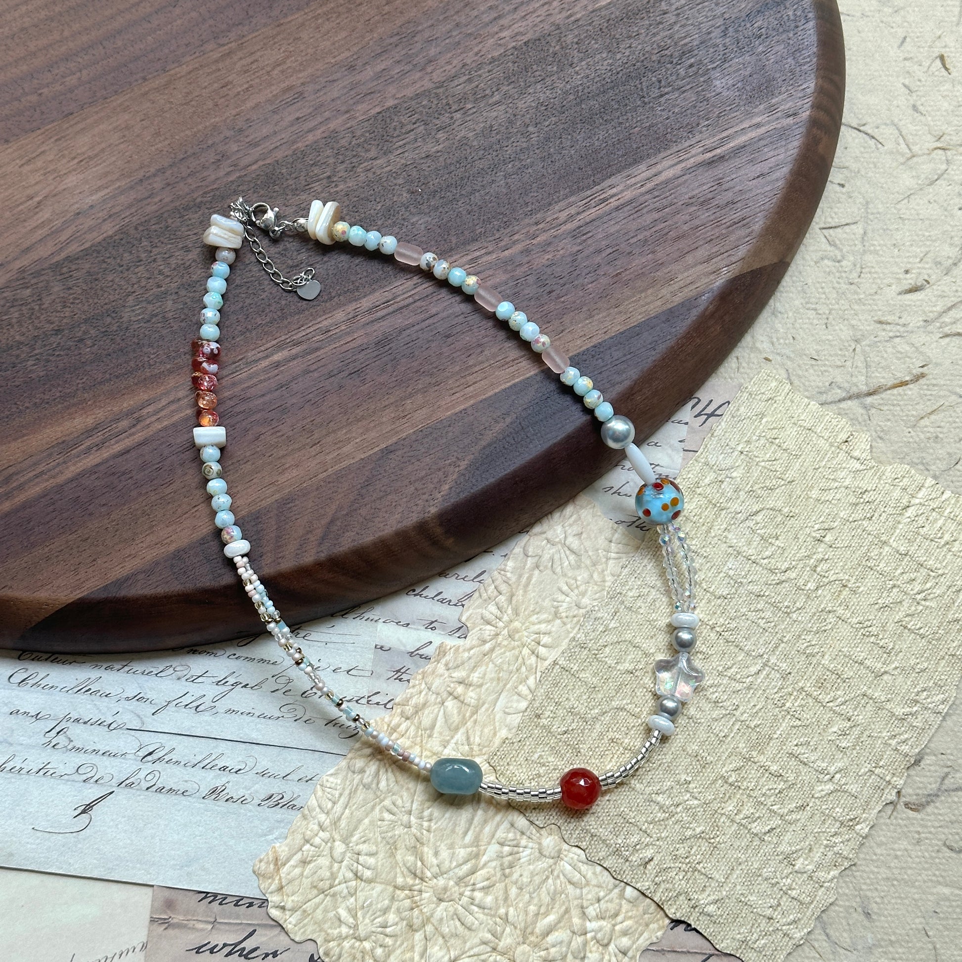 Candy Sky Necklace — circle layout on textured paper beside a wooden tray; pastel beads with red/blue accents, star charm