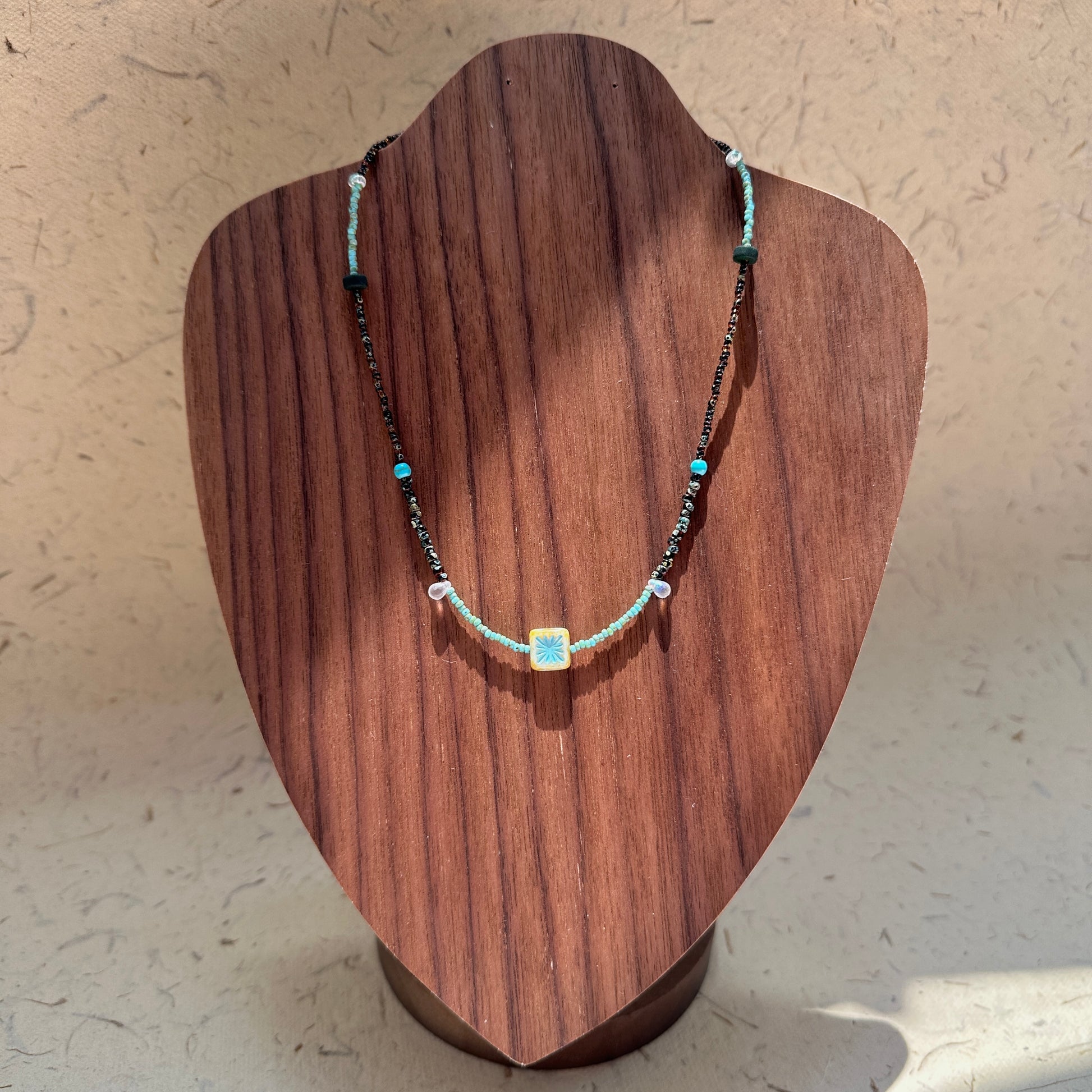 Azure Blossom Necklace on wood display bust — double-strand bronze-toned and turquoise beads with a floral ceramic charm