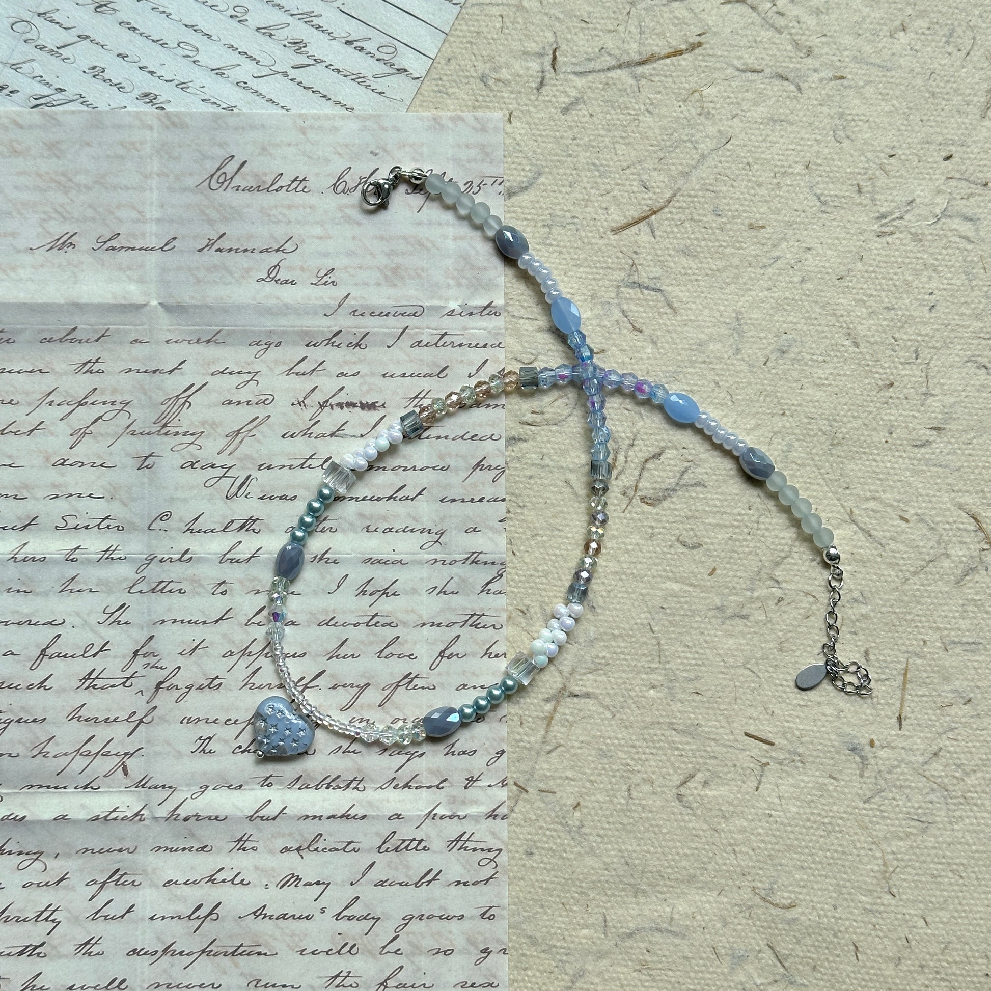 Moonlit Heart Necklace — angled view on textured paper showing bead arrangement and moonlit sparkle