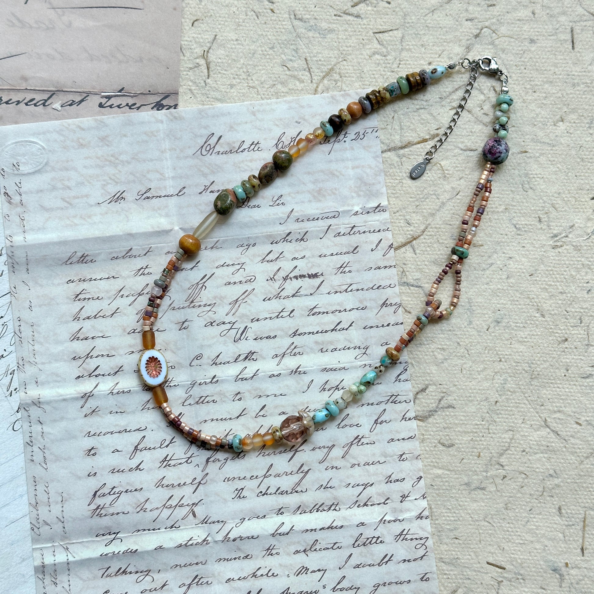 Sunlit Meadow Necklace — flat lay on vintage papers; warm amber and earthy-green glass beads with a sunflower-inspired focal