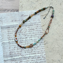 Sunlit Meadow Necklace — flat lay on vintage papers; warm amber and earthy-green glass beads with a sunflower-inspired focal