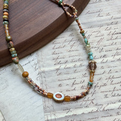 Sunlit Meadow Necklace — circle layout on textured paper; arrangement of amber and green glass beads with sunflower detail