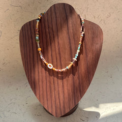 Sunlit Meadow Necklace on wood display bust — warm amber and earthy-green beads with a sunflower-inspired charm