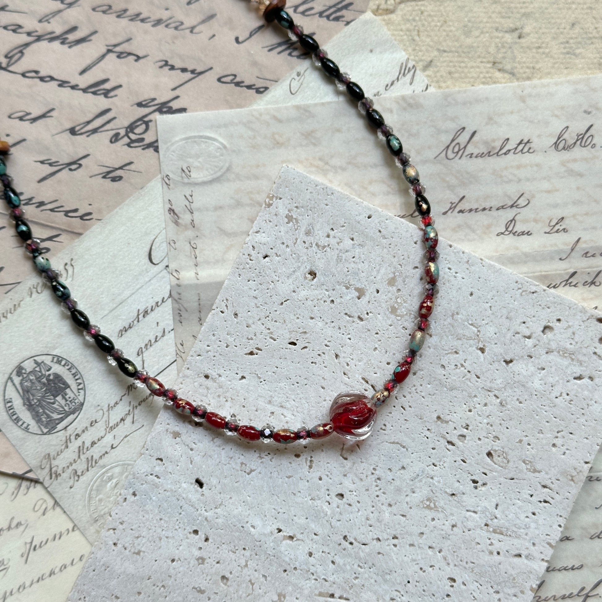 Crimson Eclipse Necklace — top-down view on round wooden tray; minimalist strand with crimson orb focal bead
