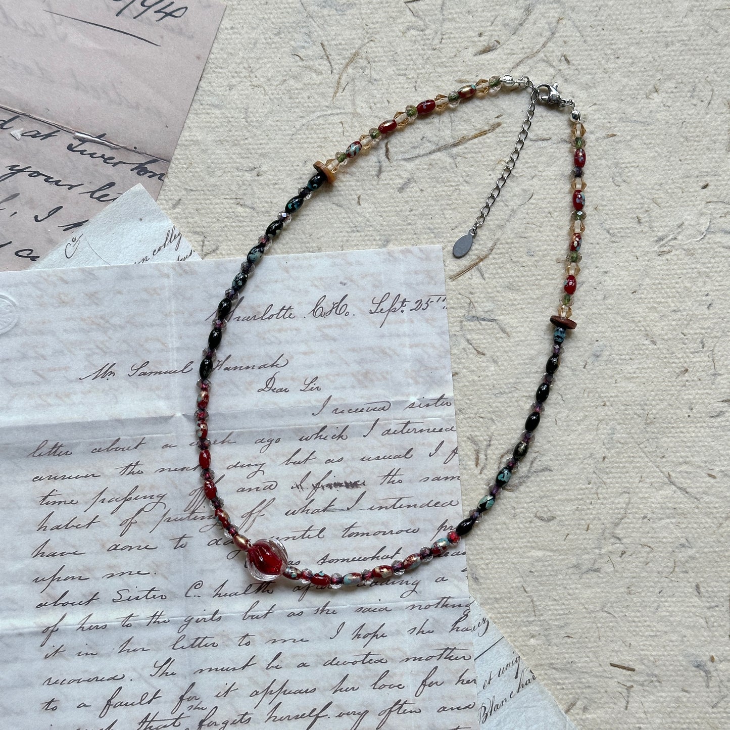 Crimson Eclipse Necklace — angled close-up on textured paper showing the crimson orb focal and bead pattern