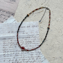 Crimson Eclipse Necklace — angled close-up on textured paper showing the crimson orb focal and bead pattern