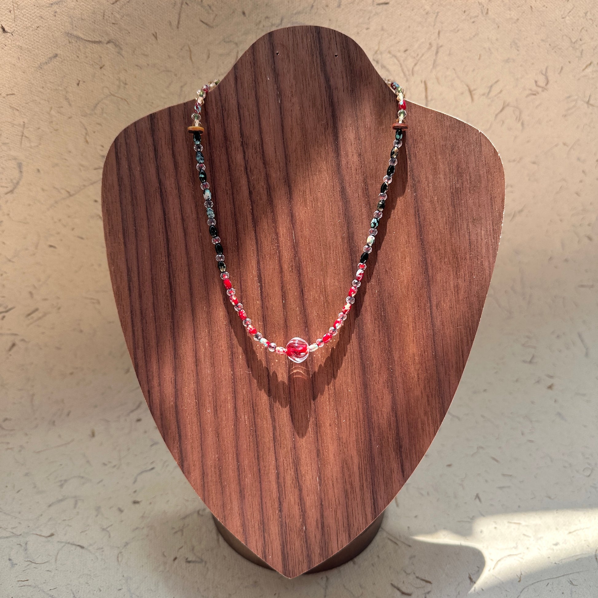 Crimson Eclipse Necklace on wood display bust — red and black glass beads with a crimson orb centerpiece