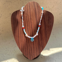 Dolphin Tide Necklace on wood display bust — seafoam-blue and pearl-white beads with a playful dolphin medallion charm