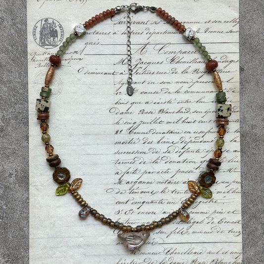 Amber Leaf Trail Necklace — flat lay on textured papers; amber/olive palette with leaf accents and clear pendant