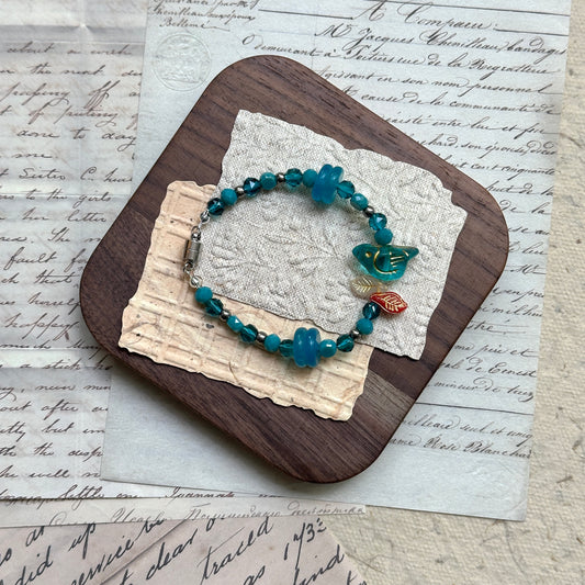 Azure Songbird Bracelet with blue glass beads and bird charm on textured background
