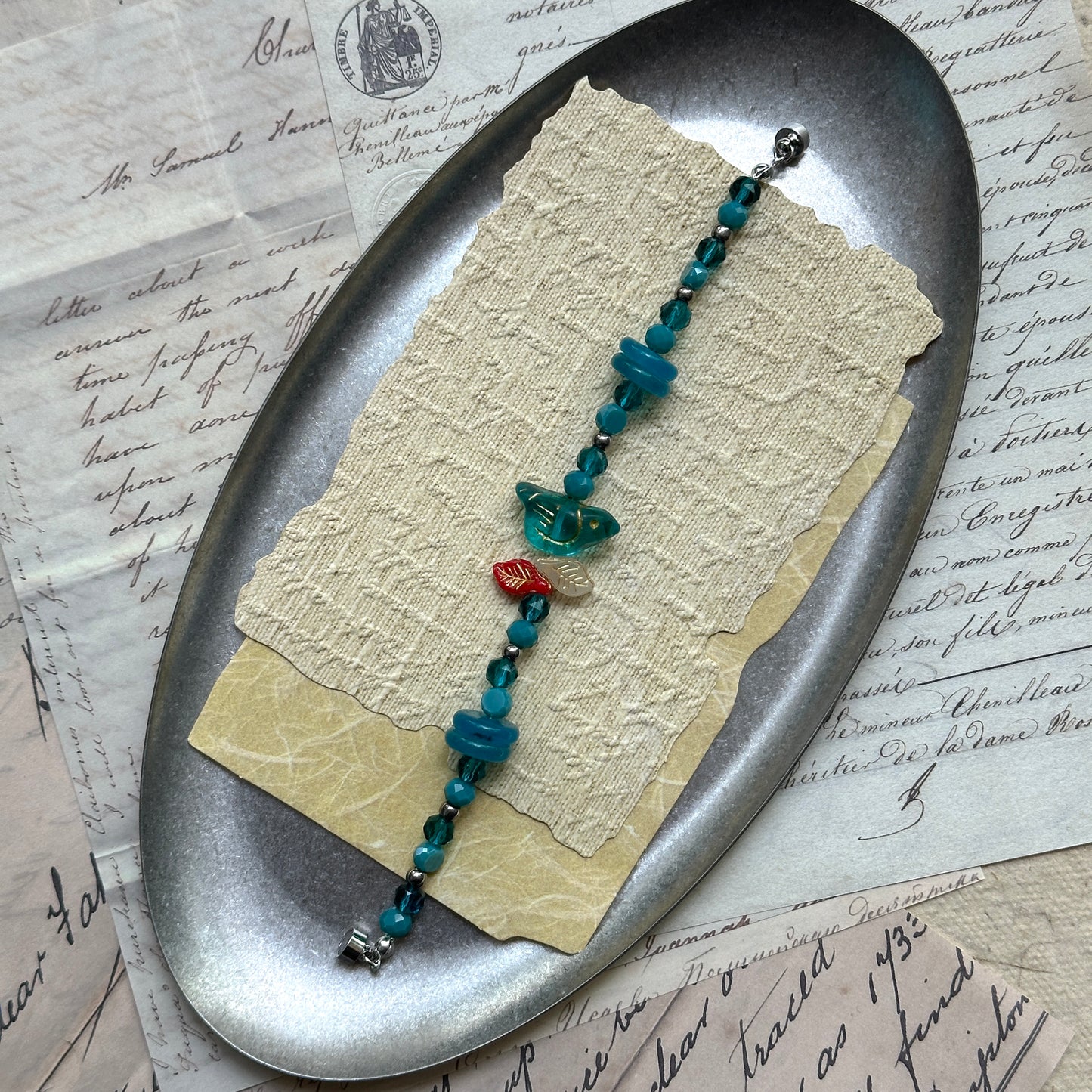 Handcrafted blue beaded bracelet with red leaf accent, nature-inspired jewelry