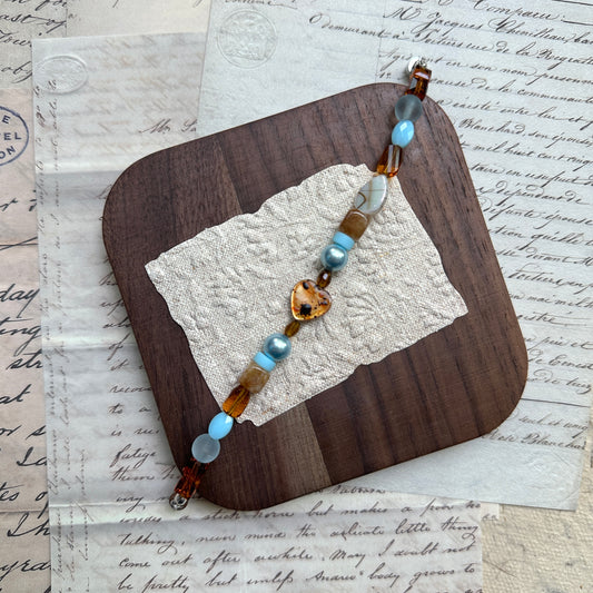 Handmade Amber Tide Bracelet with amber and blue glass beads, laid on textured stone background.