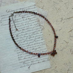 Twilight Bloom Necklace by Glazenya – handcrafted beaded necklace in wine-red, plum, and amber tones with a floral charm, displayed on vintage letter background.