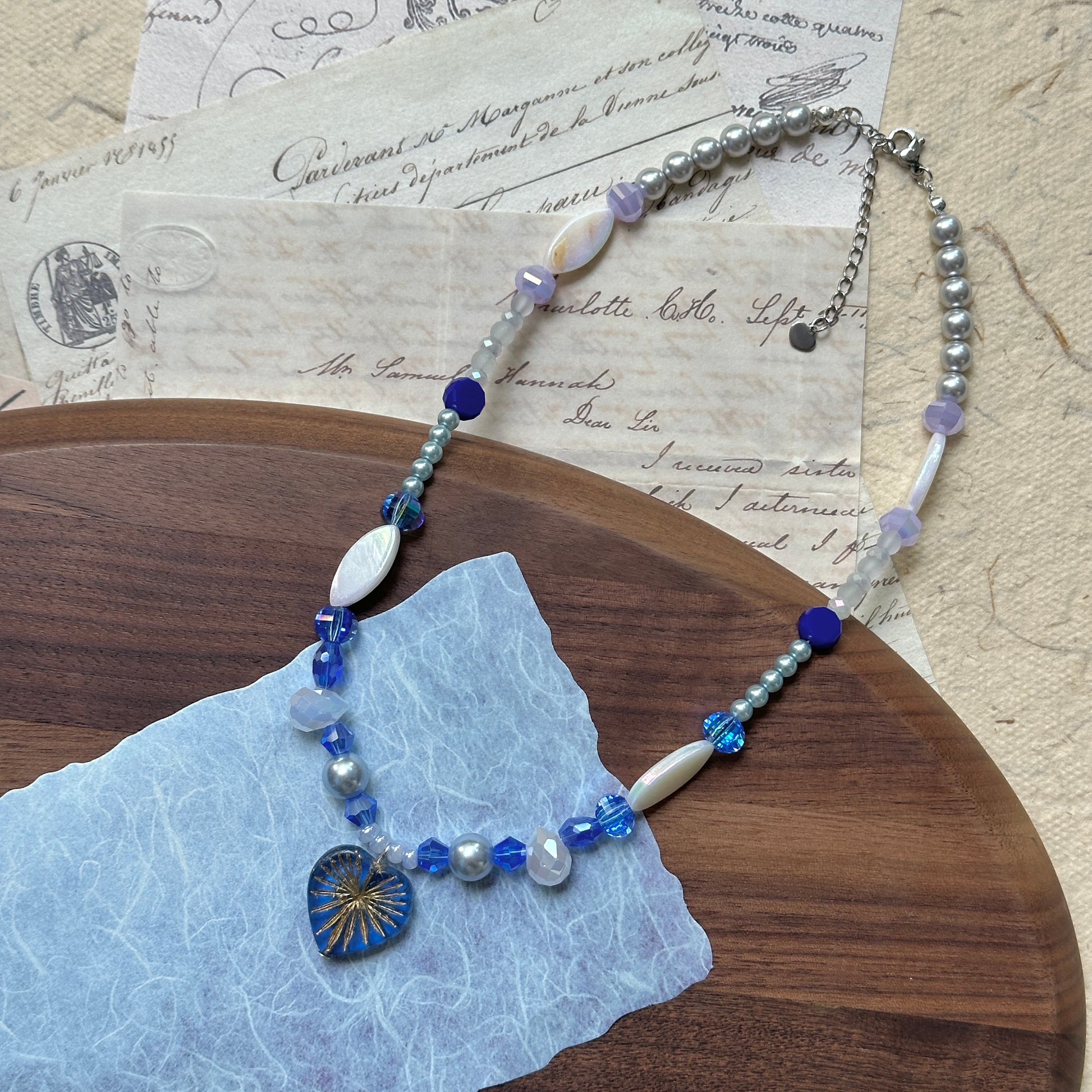 Handmade Midnight Starburst Necklace displayed on blue fabric, showcasing pearl-white and navy beads with celestial pendant