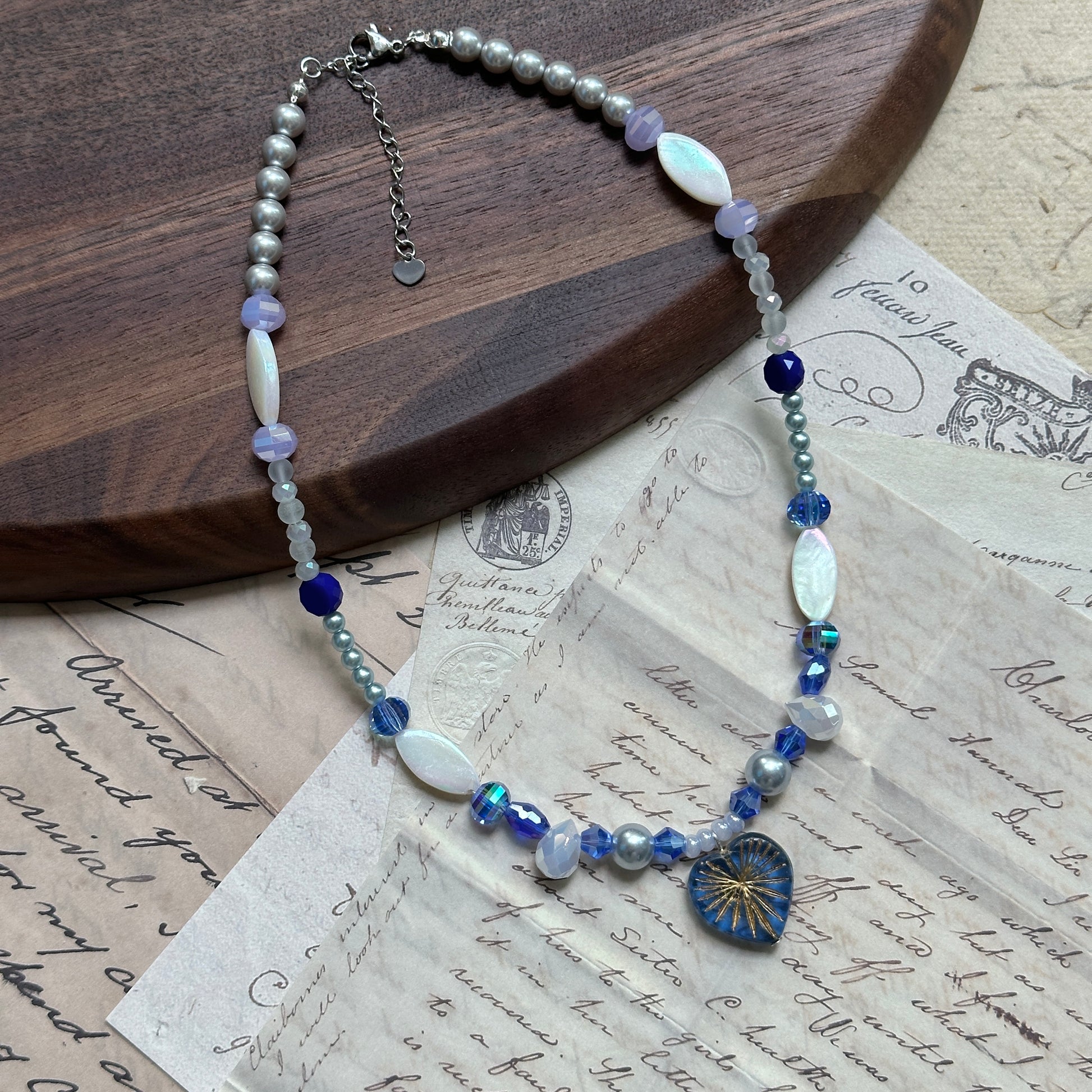 Full view of Midnight Starburst Necklace laid flat on wooden background, with glass starburst pendant and alternating navy and pearl beads