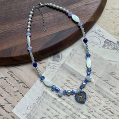 Full view of Midnight Starburst Necklace laid flat on wooden background, with glass starburst pendant and alternating navy and pearl beads