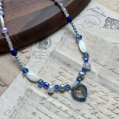 Midnight Starburst Necklace on wooden surface, featuring navy glass pendant with golden starburst motif and cobalt-blue beads