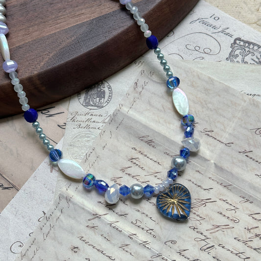 Midnight Starburst Necklace on wooden surface, featuring navy glass pendant with golden starburst motif and cobalt-blue beads