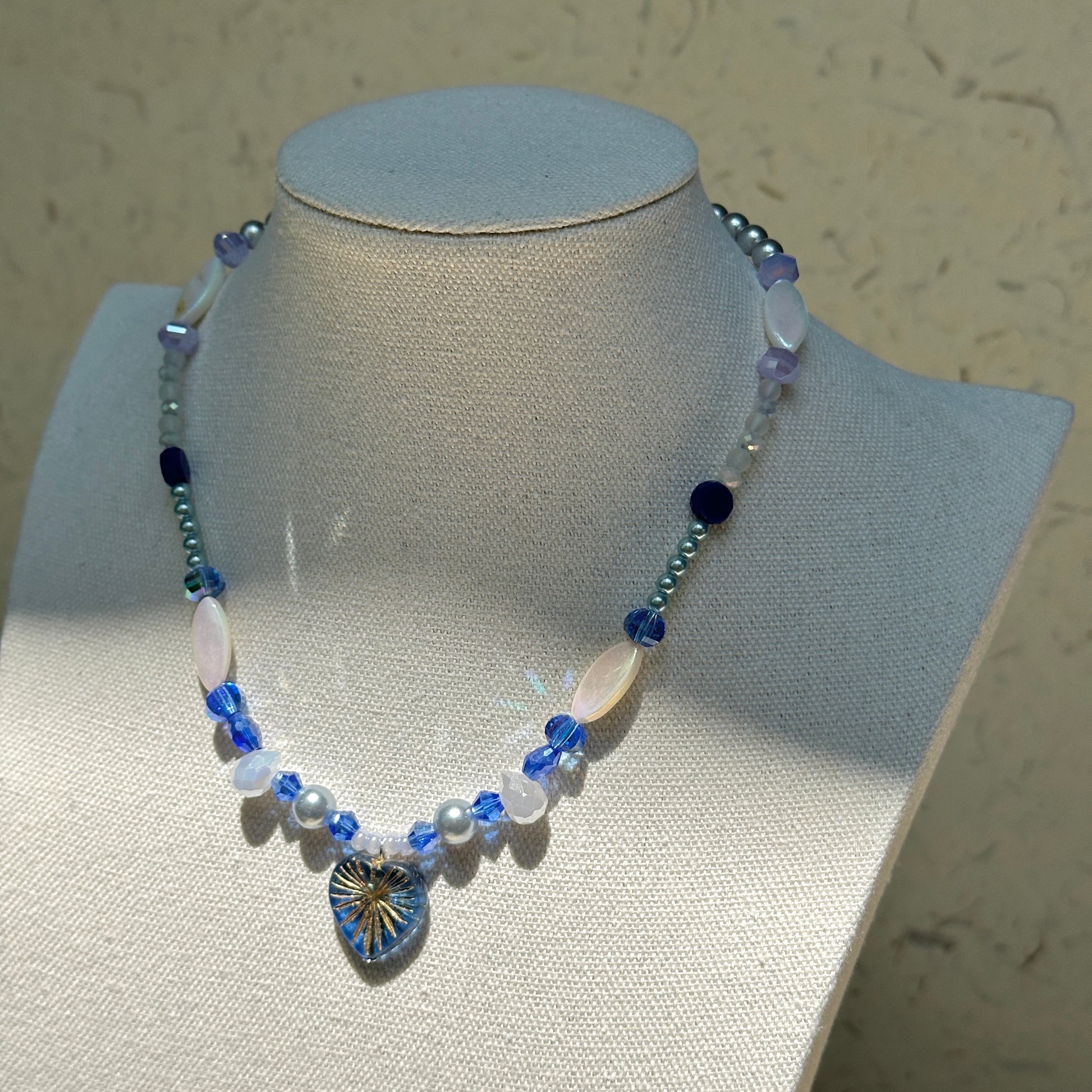 Midnight Starburst Necklace worn on display bust, highlighting elegant contrast of deep blue and pearl-white beads with golden starburst pendant