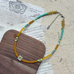 Full view of Citrus Lagoon Necklace laid flat, highlighting colorful bead palette, ceramic flower centerpiece, and amber leaf accent
