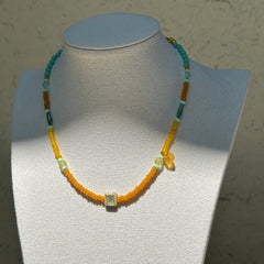Citrus Lagoon Necklace worn on bust, showcasing fresh summer palette of yellow and green beads with floral ceramic and amber leaf details