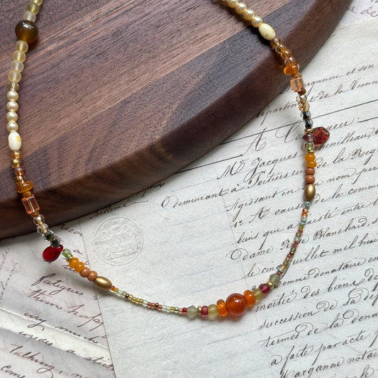 Golden Nectar Necklace close-up on wooden surface, featuring honey-amber beads, warm gold tones, and berry-red accents
