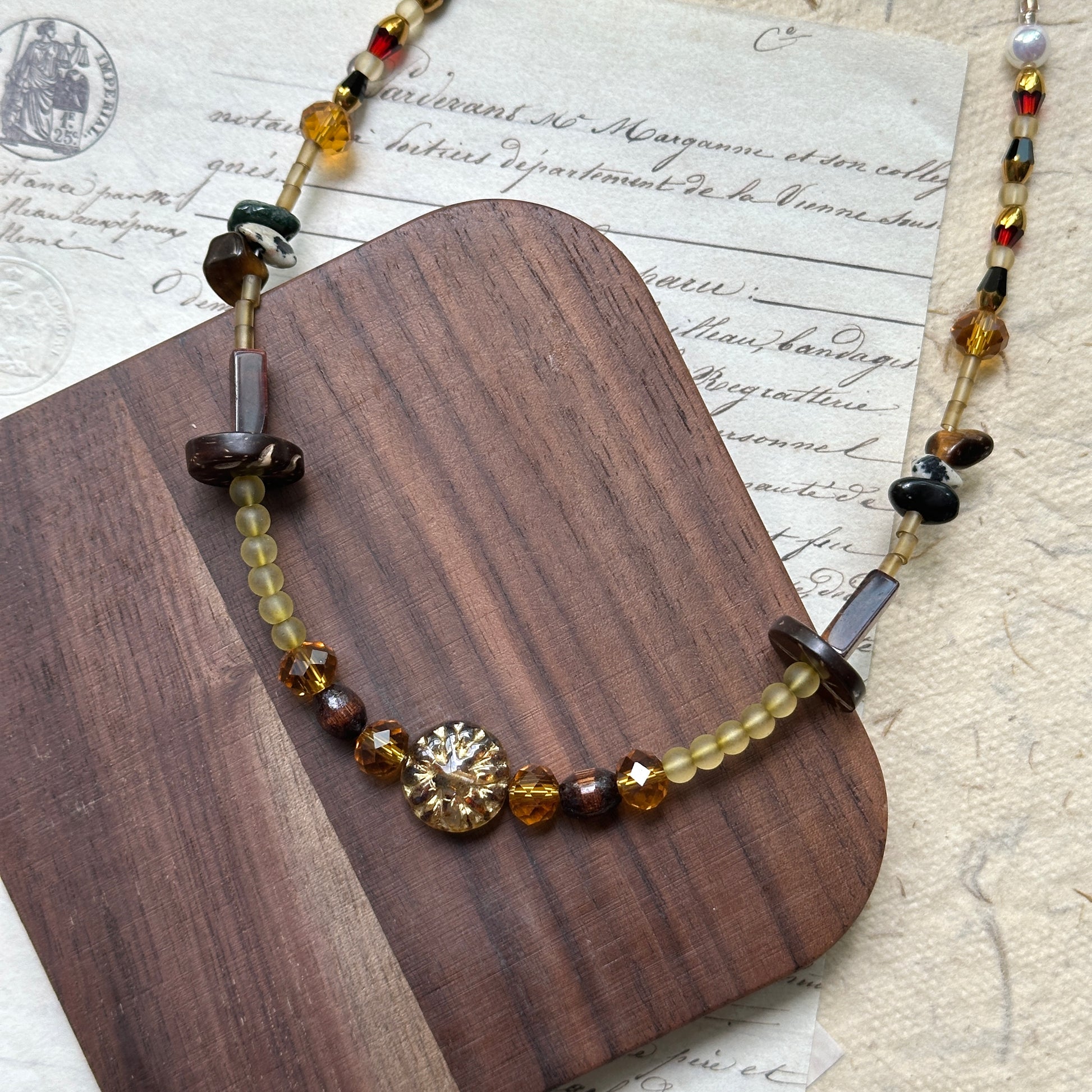 Handmade Marigold Ember Necklace with marigold and honey-amber beads, earthy brown tones, and moss-green stone accents on rustic paper background