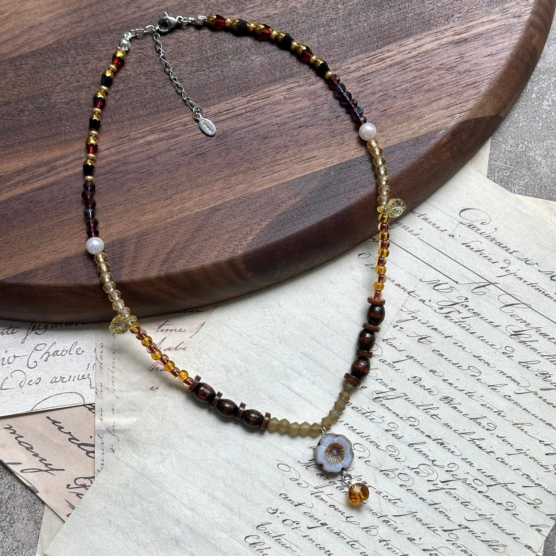 Amber Daisy Necklace displayed on wooden surface, featuring ceramic daisy pendant with amber teardrop, honey-amber beads, and brown accents