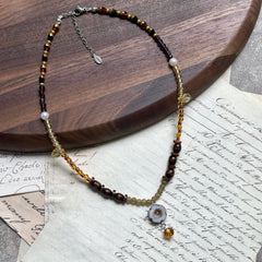 Amber Daisy Necklace displayed on wooden surface, featuring ceramic daisy pendant with amber teardrop, honey-amber beads, and brown accents