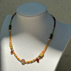 Olive Grove Blossom Necklace worn on bust, showcasing luminous glass flower pendant with earthy amber and olive-green beads
