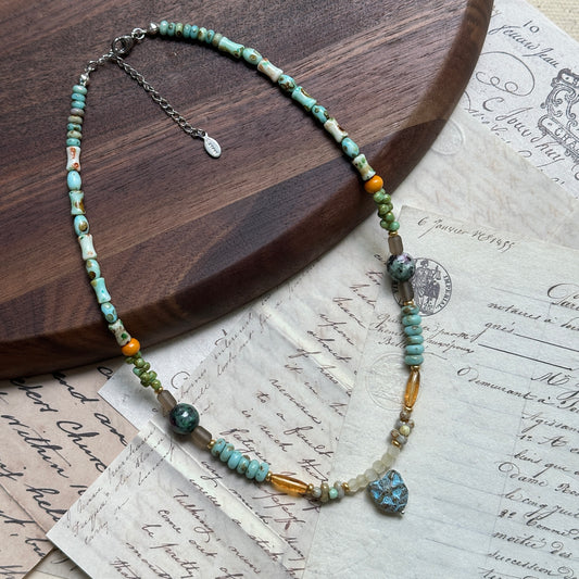 Verdant Owl Necklace close-up on wooden surface, featuring whimsical owl pendant with sage green, lagoon blue beads, creamy pearls, and gold accents