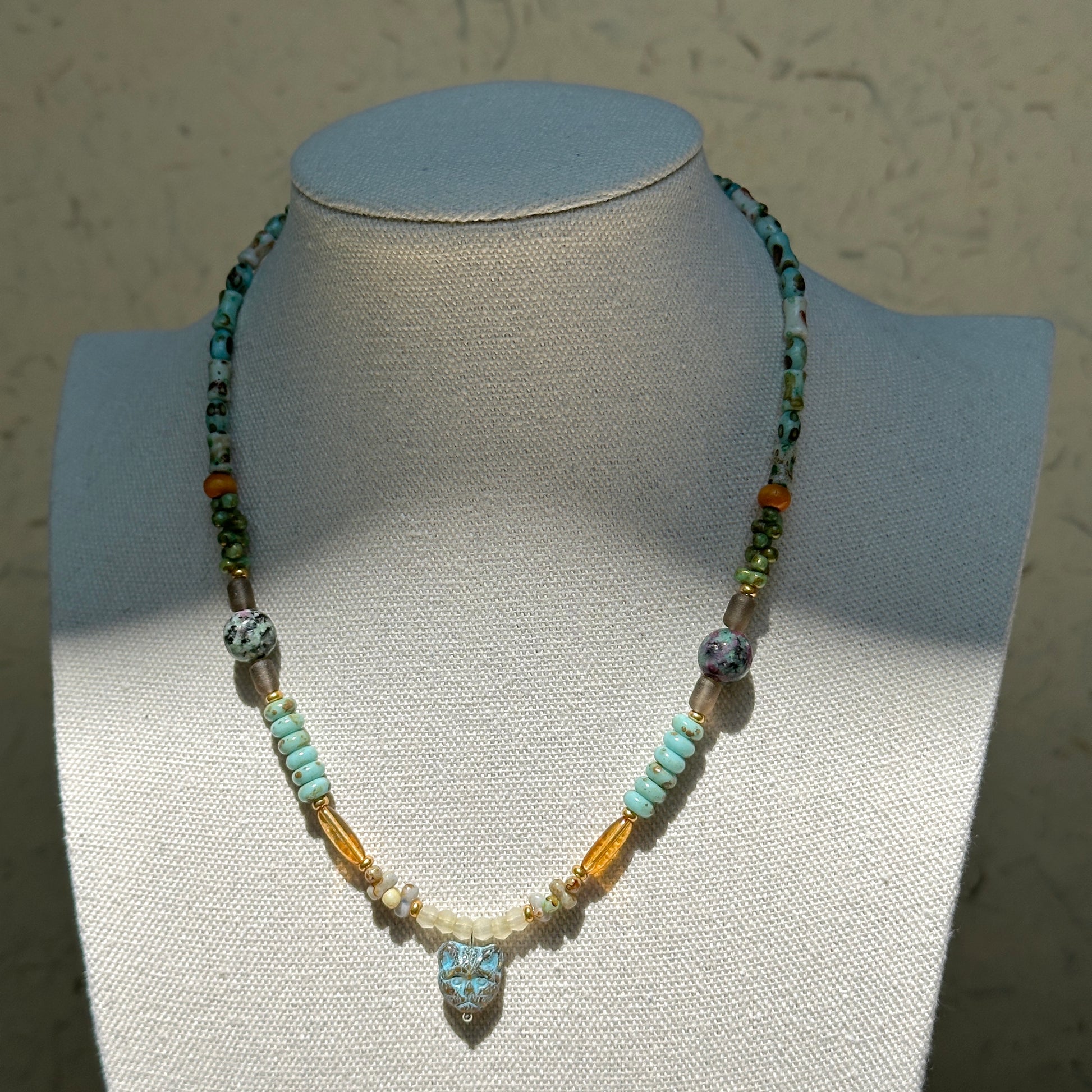 Verdant Owl Necklace worn on bust, highlighting owl pendant with harmonious mix of sage green, lagoon blue, ivory pearls, and golden accents