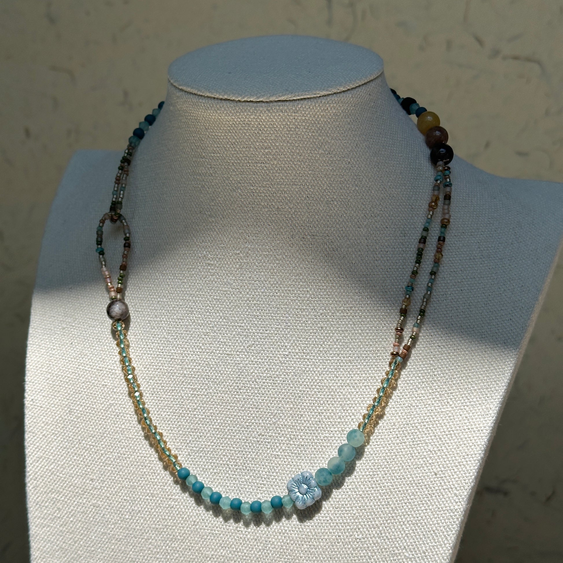 Aqua Loop Blossom Necklace worn on bust, highlighting asymmetrical double-loop side detail with aqua and gold beads and floral glass centerpiece